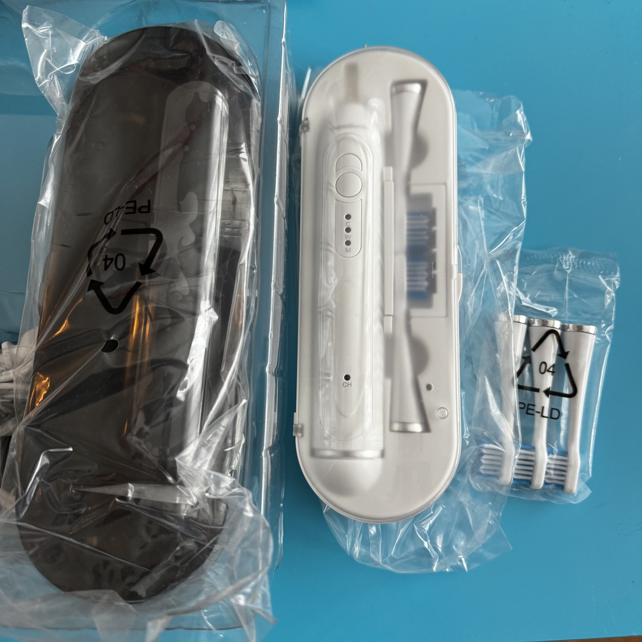 Unboxed contents of the AquaSonic Duo Series toothbrush set and accessories, including two sonic toothbrush handles, travel cases, and multiple brush heads. Each brush has five heads, with two heads pre‑packaged in its corresponding case.